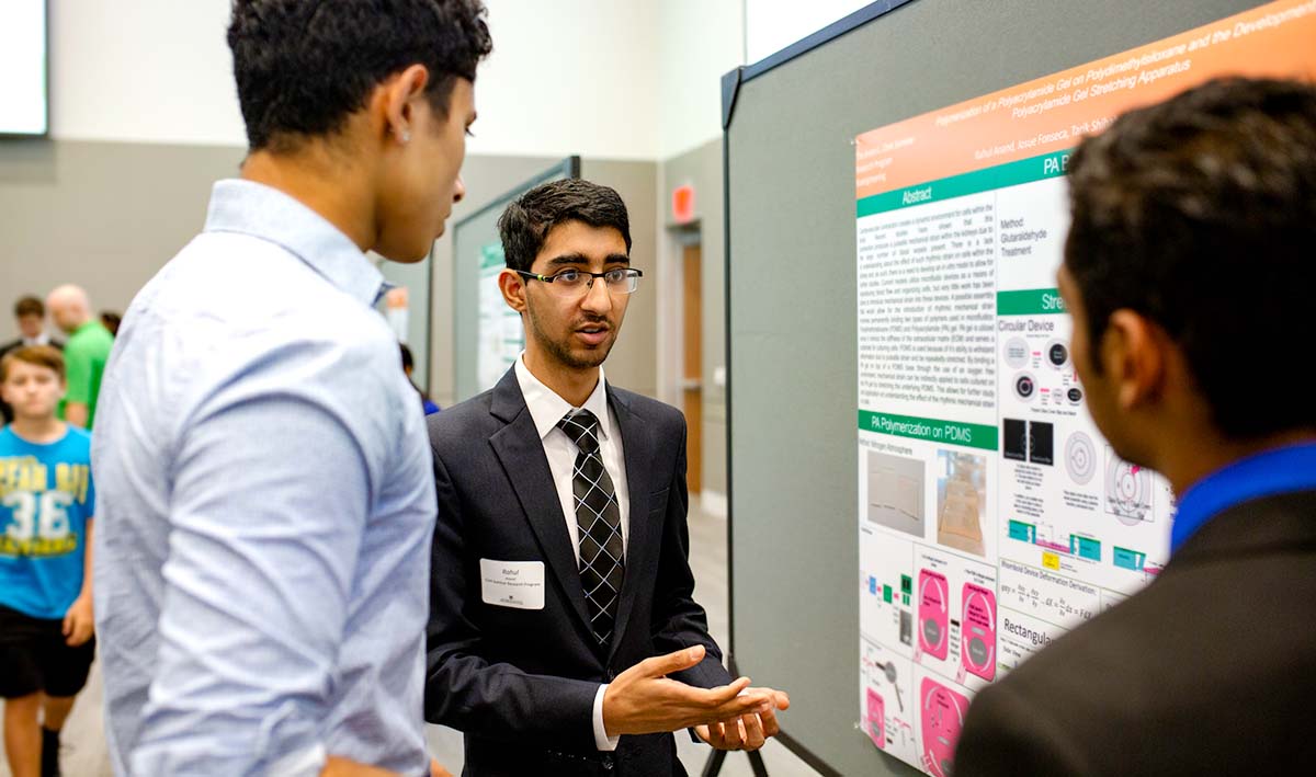 A student discussing research poster with two others.