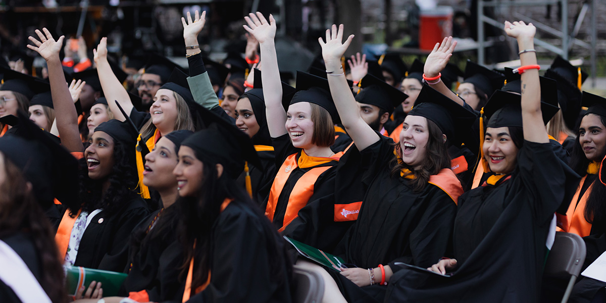 a crowd of graduates raising their hands during commencement